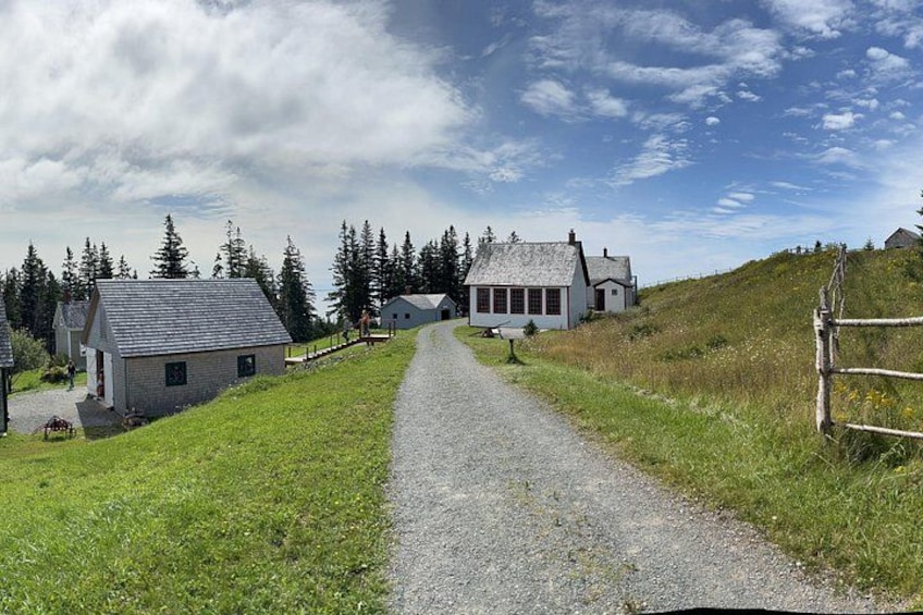 A gravel path leading to a cluster of houses on a grassy hill with a clear sky. 3