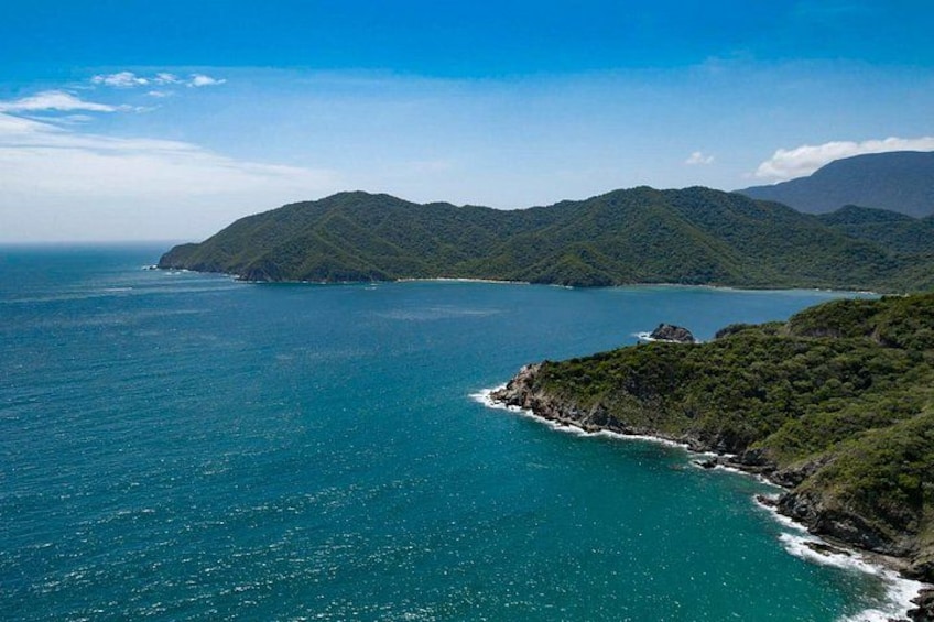 Un paisaje costero con mar azul cristalino, colinas verdes y un edificio pequeño a la derecha. 4