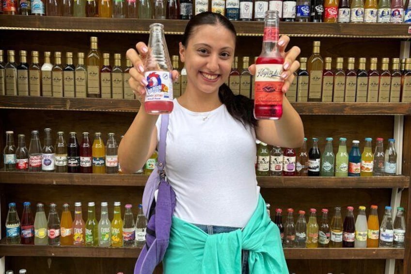A person holding two bottles of beverage in front of a shelf stocked with various bottles. 5