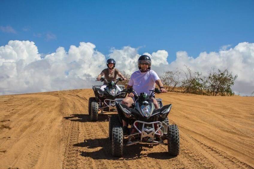 Two people riding quad bikes on a sandy trail with a clear sky. 1