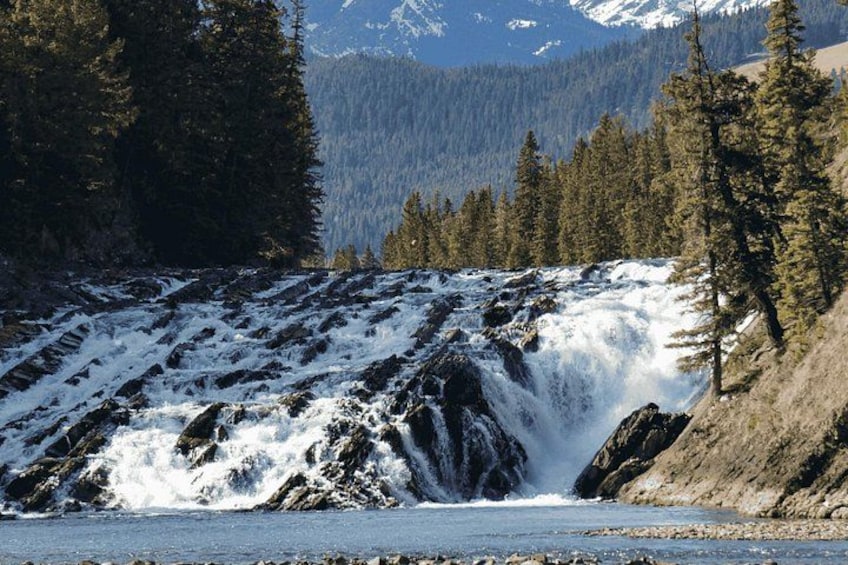 A waterfall cascading over rocks, surrounded by dense forest and mountains in the background. 2