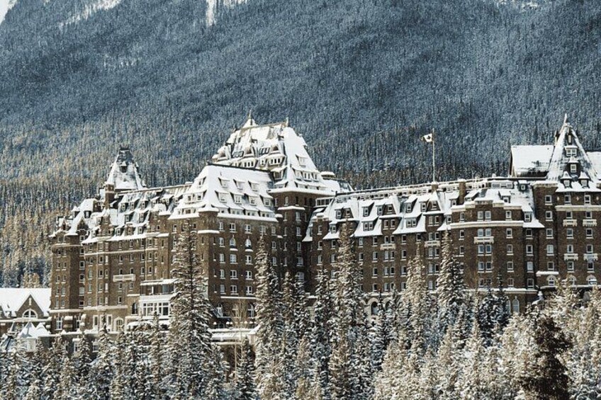 A large, historic building with snow-covered roofs, surrounded by dense forest and mountains. 3