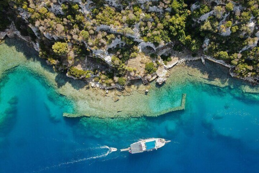 An aerial view of a boat on turquoise waters surrounded by rocky cliffs and sparse vegetation. 1
