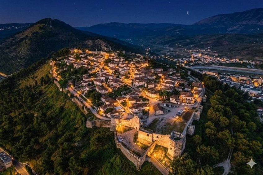 A town nestled in a valley at night, surrounded by hills, with a prominent castle-like structure. 1
