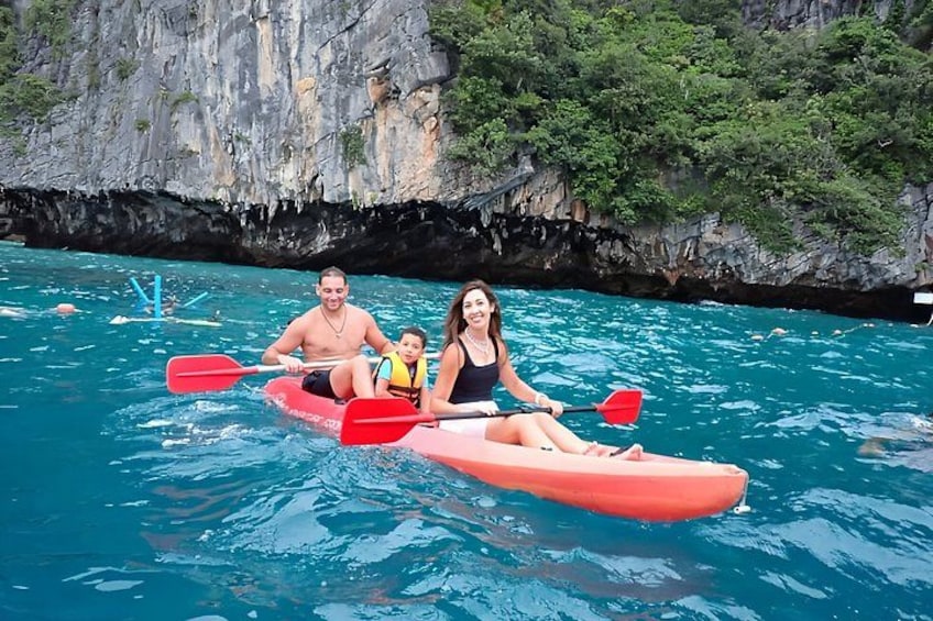 Una famiglia fa kayak su un mare turchese, con alte scogliere rocciose sullo sfondo. 4