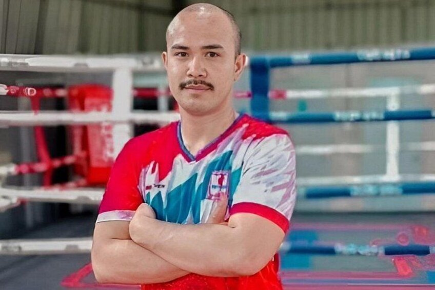A person standing in a boxing ring with boxing gloves and equipment in the background. 2
