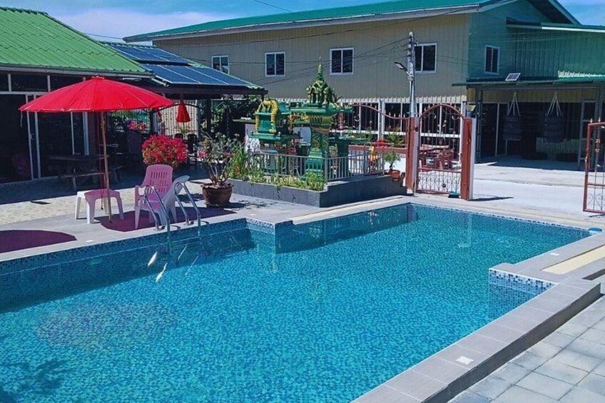 A swimming pool with a red umbrella, chairs, and potted plants. 3