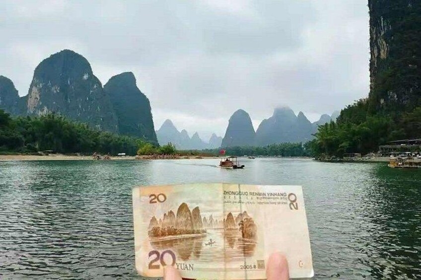 En 20 yuan note holdes foran en flod med både og kalkstensformationer i baggrunden. 1