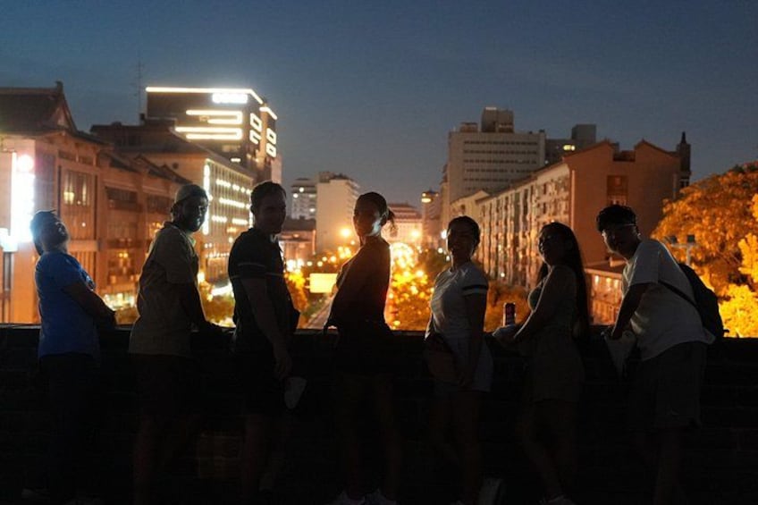 A group of people standing on a bridge at night with city lights in the background. 3