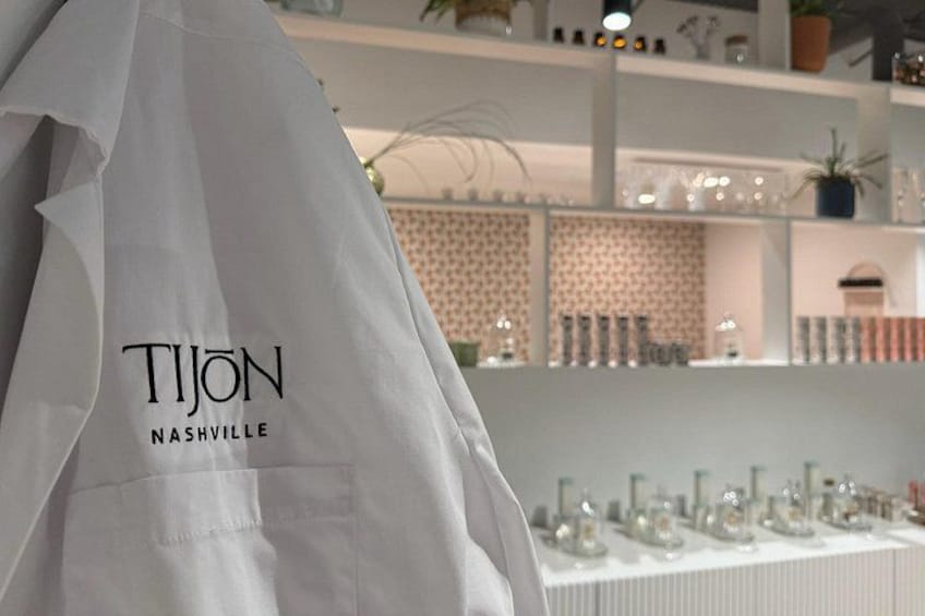 A white Tiyon Nashville apron hanging in a store with shelves in the background. 4