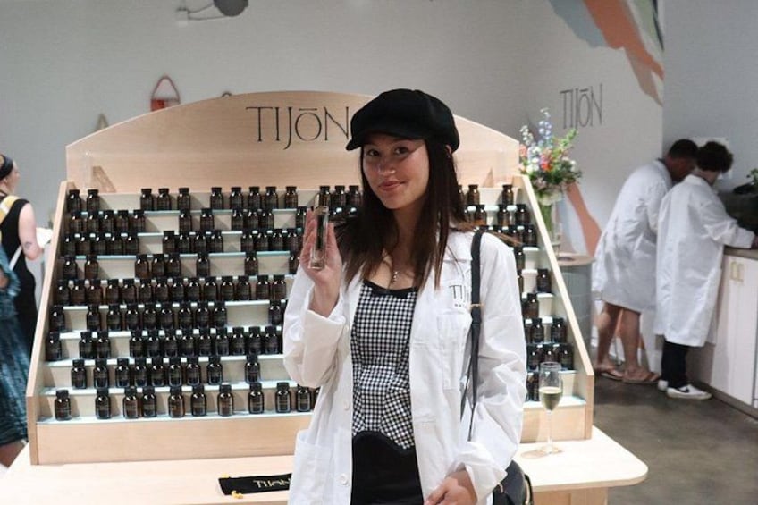 A person standing in front of a display of bottles, with a sign that reads 'TIJON' in the background. 3