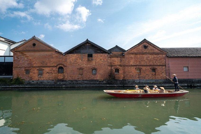 A traditional boat with passengers, a brick building, and a calm river. 3