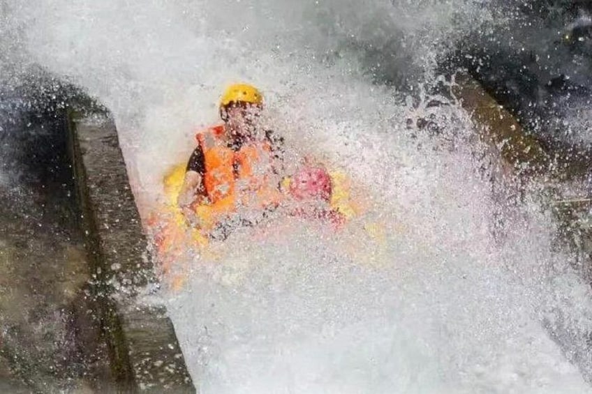 A person in a yellow helmet and orange life jacket navigating through a turbulent water body. 2