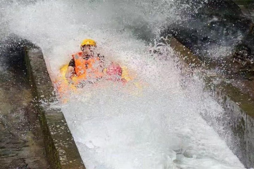A person in a yellow helmet and orange jacket navigating a turbulent water channel. 5