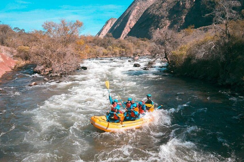 Un groupe de personnes fait du rafting sur une rivière, entourée de falaises rocheuses et d’une végétation clairsemée. 4