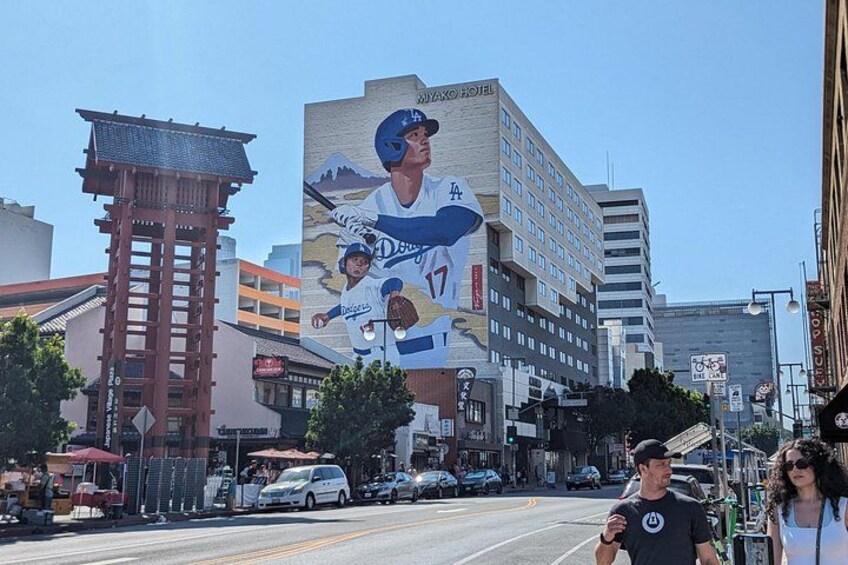Calle con un gran mural de jugadores de béisbol en un edificio, un tradicional torii japonés y edificios modernos. 4