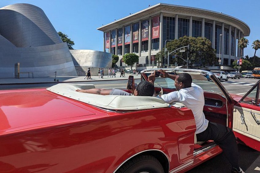 Un coche descapotable rojo con un hombre conduciendo, un edificio moderno y una estructura curva al fondo. 5