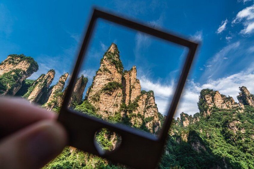 A hand holding a photo frame with a landscape of tall, narrow rock formations and lush greenery. 1