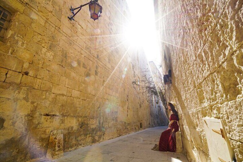 Une ruelle étroite où l’on aperçoit une personne vêtue d’une robe rouge, appuyée contre un mur. 3