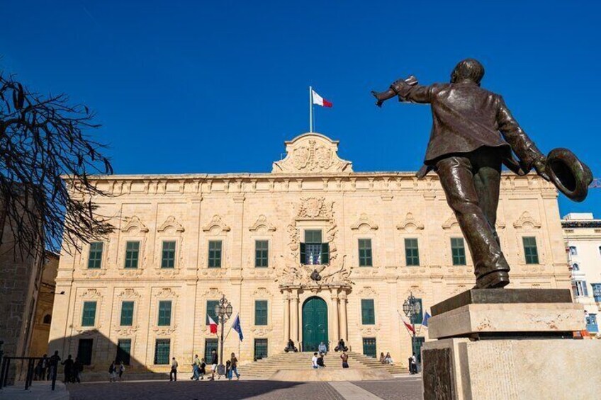 Un grand bâtiment devant lequel se trouve une statue d’un homme tenant un chapeau. 1