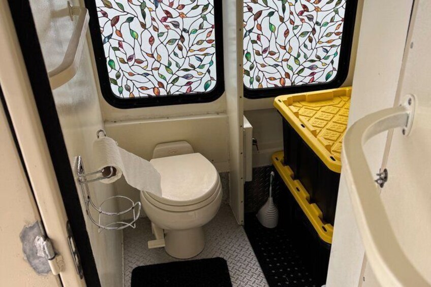 A compact bathroom with a toilet, a yellow storage bin, and a patterned window. 2
