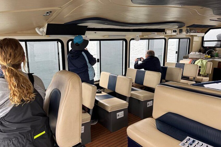 Interior de barco con asientos, una persona tomando una foto y otra mirando por la ventana. 3