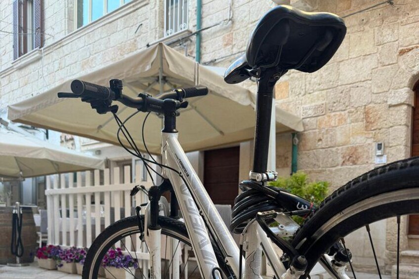Una bicicleta estacionada frente a un edificio con cerca blanca y un paraguas color beige. 3