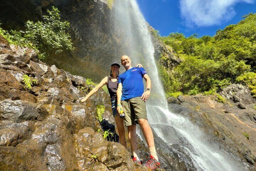 Een man en vrouw staan bij een waterval in een rotsachtig gebied met weelderige begroeiing. 5