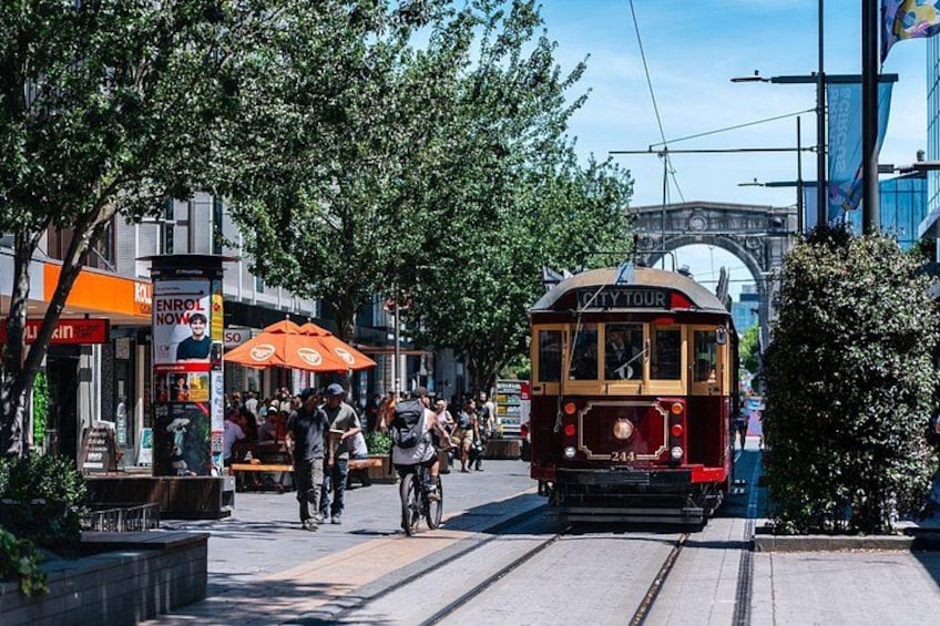 Un tranvía sobre rieles, personas caminando y una parada de tranvía con un paraguas naranja. 5