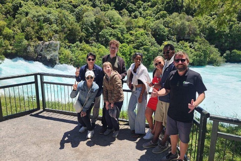 A group of people standing on a concrete platform overlooking a river with a rocky outcrop in the background. 2