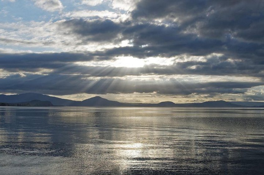 A calm body of water reflecting sunlight, with mountains in the background and a cloudy sky. 4