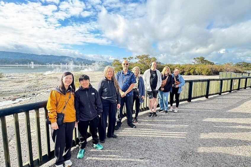 A group of people standing on a paved walkway by a body of water with a wooden railing. 3