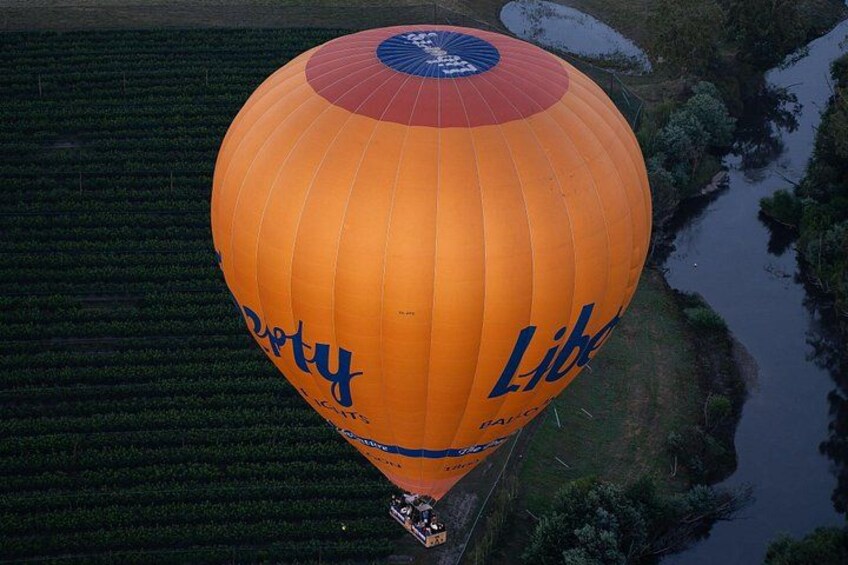 A hot air balloon with 'Depty' and 'Liberty' written on it, flying over a field with a river. 5
