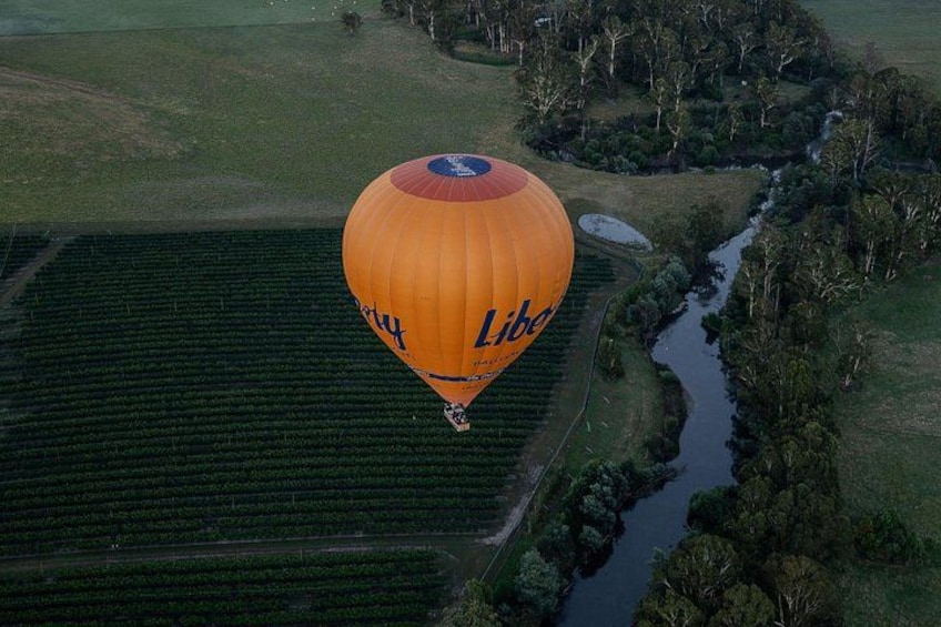 A hot air balloon over a rural landscape with fields and a river. 2