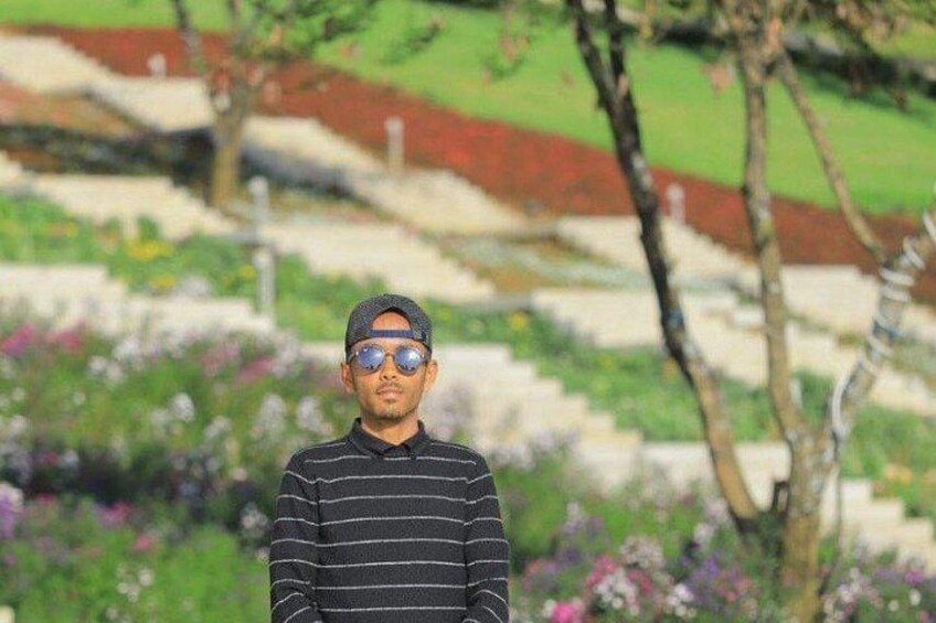A person standing in a garden with a striped shirt, surrounded by greenery and flowers. 4