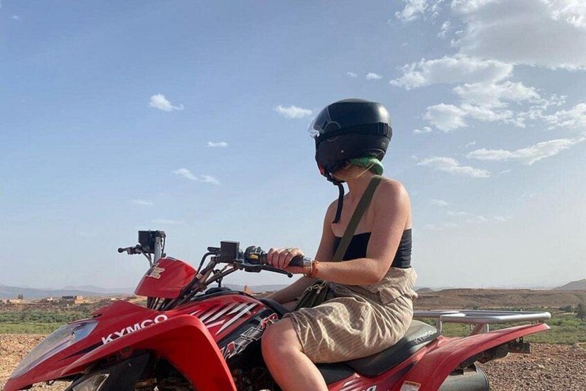 En person kører på en rød ATV med hjelm og grønt bandana i et landligt landskab med bakker og en klar himmel. 5