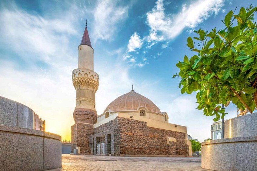 A mosque with a tall minaret and a dome, surrounded by stone walls and potted plants. 3
