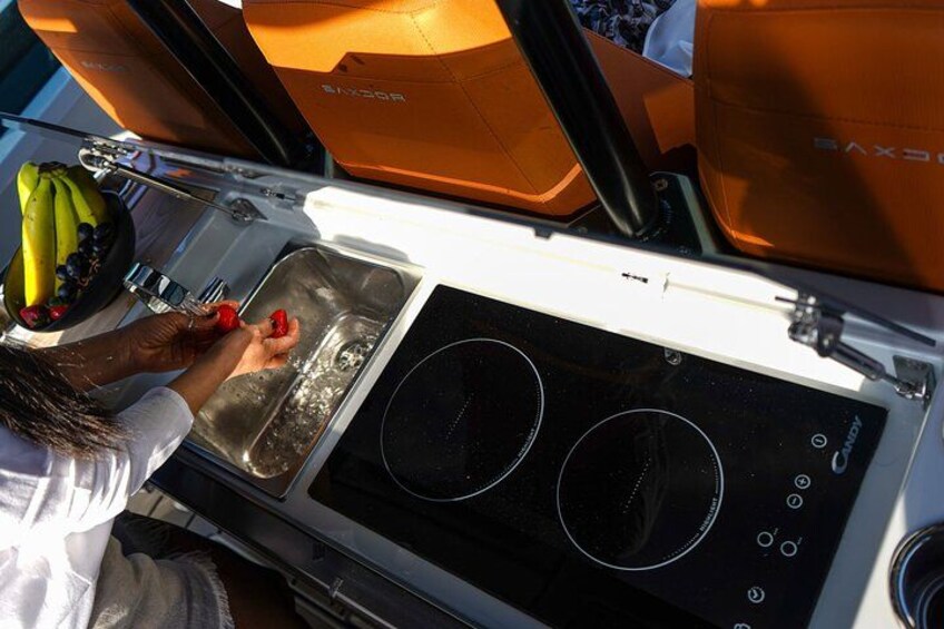 A woman washing fruits in a boat's galley, with a stove and sink visible. 3