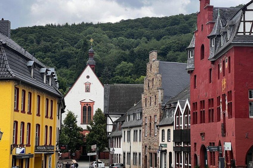 A street with colorful buildings, a church, and a forested hill in the background. 4