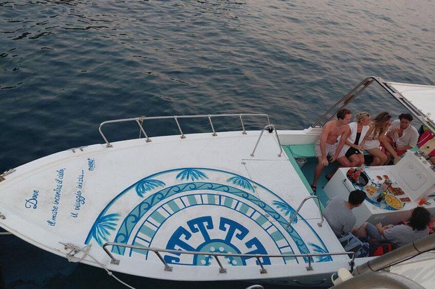 Ein Boot mit Personen an Bord, ein kreisförmiges Logo und Schriftzug an der Seite. 1