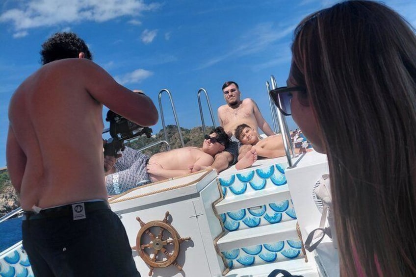 A boat with people sunbathing on the deck, a steering wheel, and a railing. 5