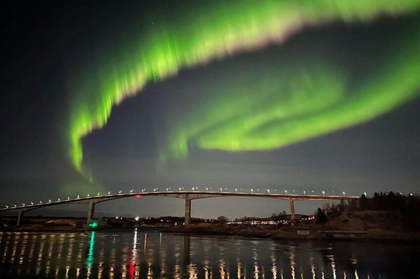 A bridge with lights reflecting on water, and the aurora borealis in the background. 3