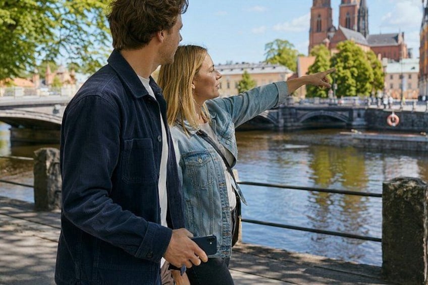 A couple standing by a river with a bridge and buildings in the background. 5