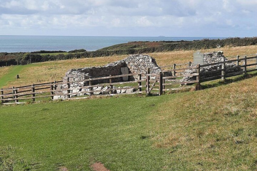 Ancient stone ruins, a wooden fence, and a grassy field with a view of the sea. 3