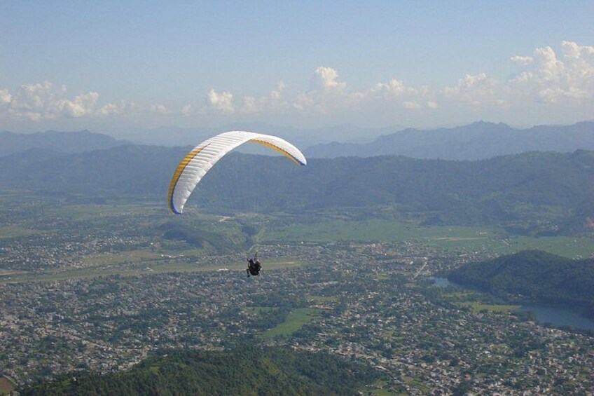 A person paragliding over a cityscape with mountains in the background. 4