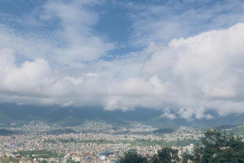 A cityscape with a mountainous backdrop under a partly cloudy sky. 2