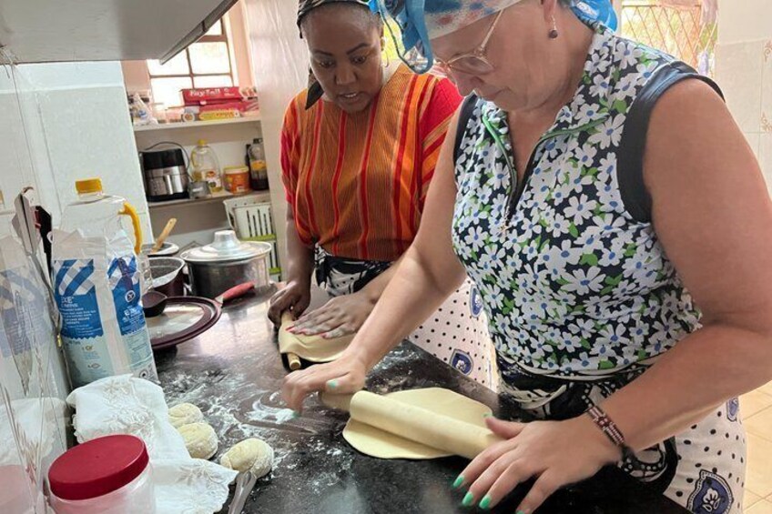Two people rolling dough on a kitchen counter with flour scattered around. 1