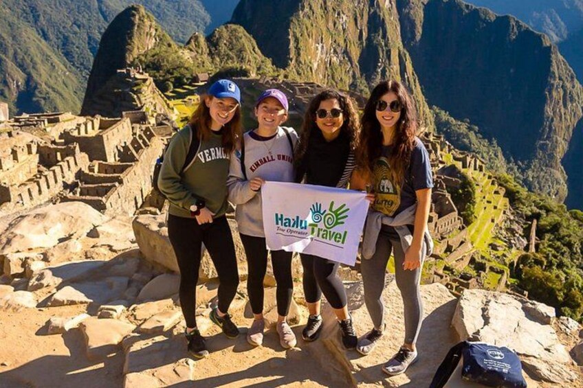 Four people standing on a stone pathway with a mountainous landscape in the background. 4