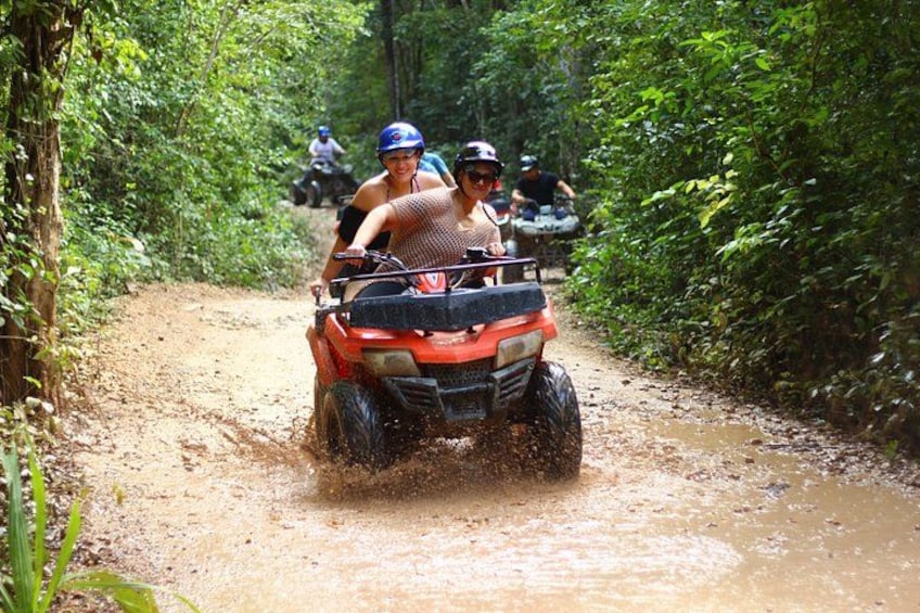 A person riding an ATV on a muddy path surrounded by dense vegetation. 5