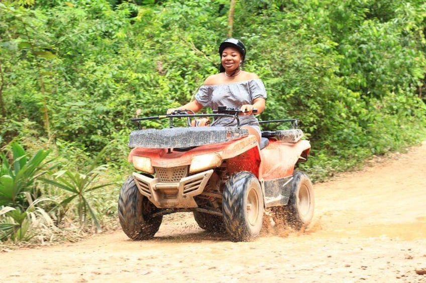 Une personne conduisant un véhicule tout-terrain sur un chemin de terre, entourée d’une végétation luxuriante. 4